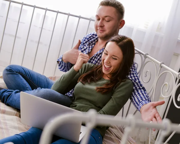 Young couple using a laptop lying on their bed — Stock Photo, Image