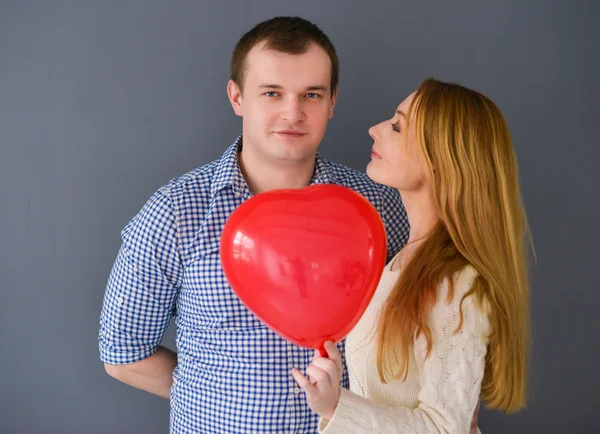 Schönes verliebtes Paar mit rotem Ballon in Herzform zum Valentinstag, auf grauem Hintergrund — Stockfoto