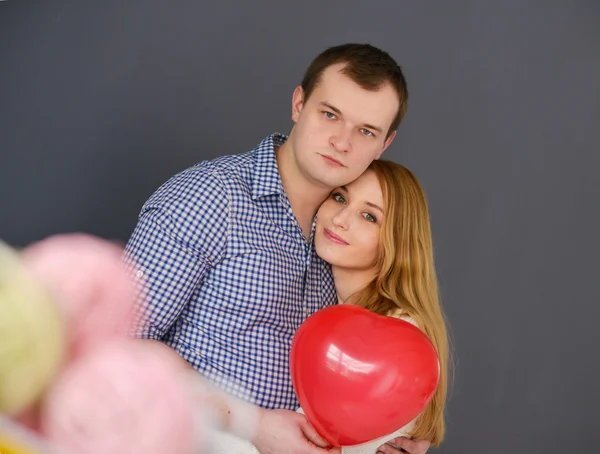 Schönes verliebtes Paar mit rotem Ballon in Herzform zum Valentinstag, auf grauem Hintergrund — Stockfoto