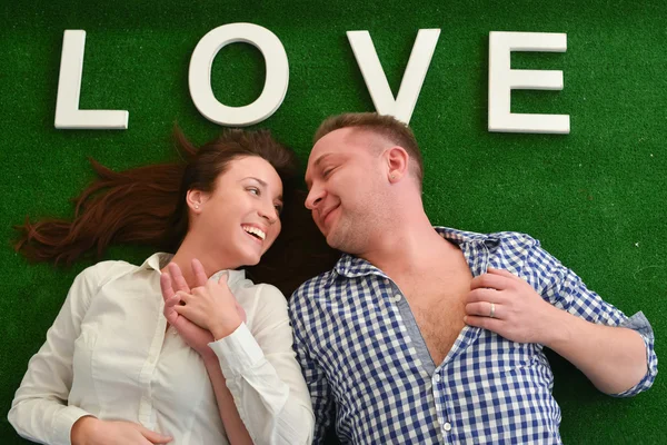 Feliz joven pareja acostada sobre una alfombra verde — Foto de Stock