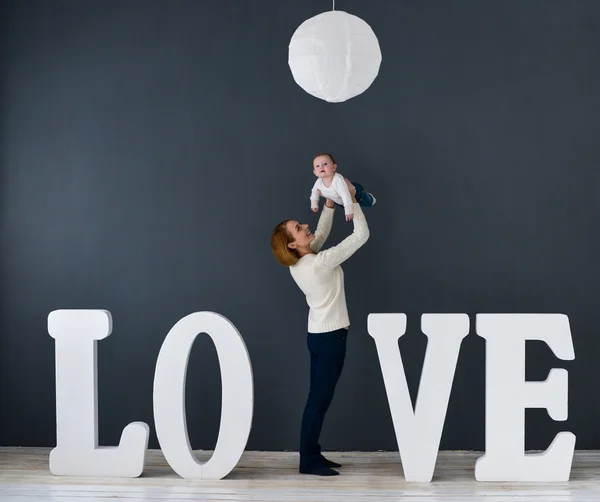 Portret szczęśliwy matki i dziecka, na szarym tle w pobliżu dużych liter słowa miłości — Zdjęcie stockowe