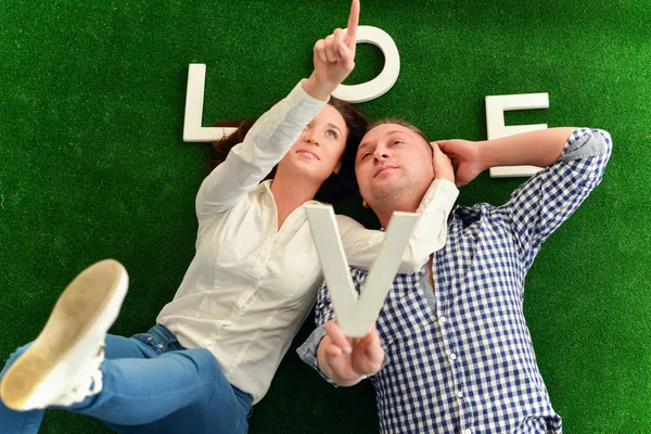 Šťastný mladý pár ležící na zádech přes zelený koberec — Stock fotografie