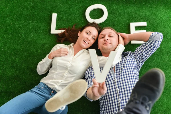 Feliz joven pareja acostada sobre una alfombra verde — Foto de Stock