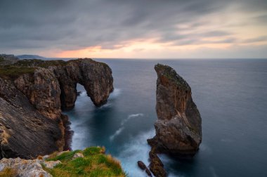 İspanya, Asturias, Ribadesella yakınlarındaki Acantilados del Infierno 'da günbatımında Punta Pena Flecha' da doğal kemer. Canlı günbatımı renkleriyle harika doğa manzarası.