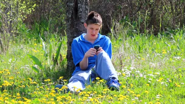 Хлопчик з мобільним телефоном. Хлопчик-підліток сидить на відкритому повітрі за допомогою мобільного телефону — стокове відео