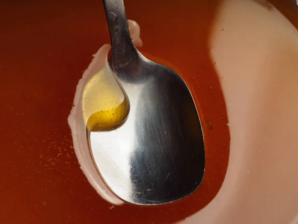 Metal spoon on surface of honey. Reflection of light on honey surface. Honey flowing in into the spoon. Close-up view. Macro shot. — Stock Photo, Image