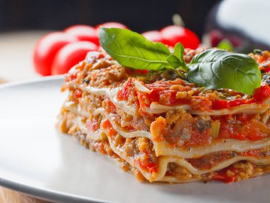 Arka planda fesleğen yapraklı ve domatesli lazanya parçasına ekstra yakın görüş. İtalyan mutfağı menüsü.