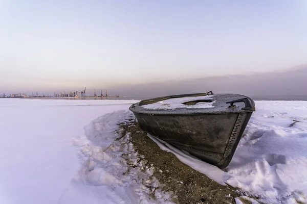 an old fishing boat lies in the snow on the shore of a frozen sea without people