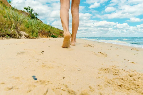 man's naked legs walks barefoot along the beach towards the city