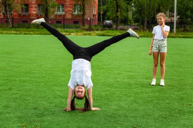 Kız stadyumda akrobasi yapıyor. Isınma, ayağa kalkma, çocuk, sokak, gündüz