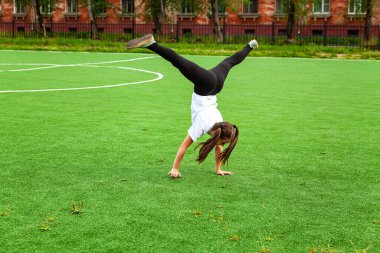 Kız stadyumda akrobasi yapıyor. Isınma, ayağa kalkma, çocuk, sokak, gündüz