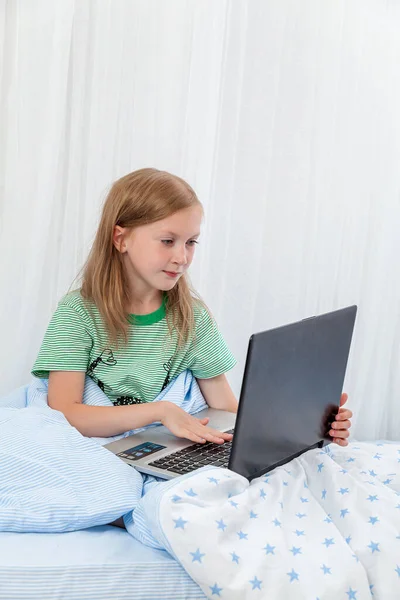 A girl sits on a bed with a laptop. Distance learning. Lessons. homework. education. Home schooling