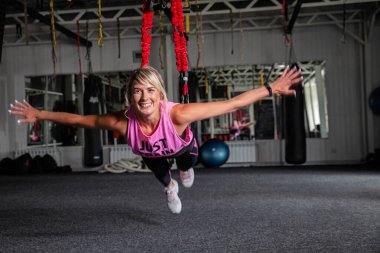 Bungee fitness. Döngüler üzerinde çalışıyorum. Pembe eşofmanlı güzel bir spor kadın spor salonunda özel döngülerin yardımıyla antrenman yapıyor. Araf 'ta pozlar