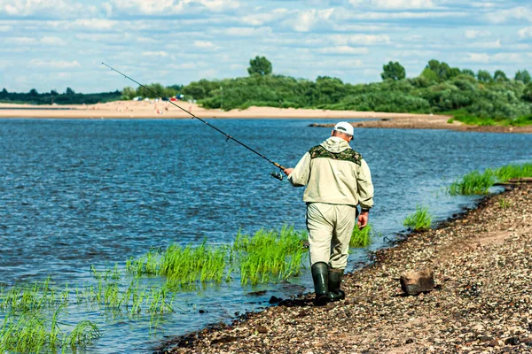 川で釣り 釣りだ スピニング 釣り竿を手に男の漁師が川岸を歩いている — ストック写真