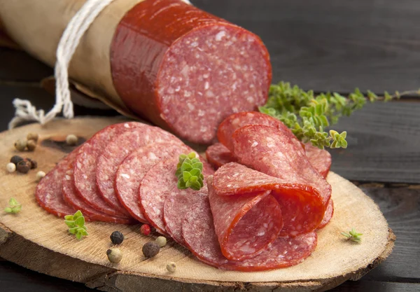 Halbiert in Scheiben köstliche Salami serviert auf einer Scheibe Holz mit Thymian und gemahlenem Pfeffer lizenzfreie Stockbilder