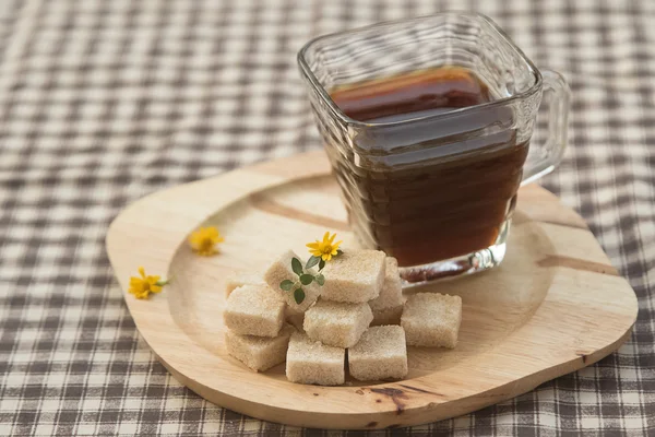 Bruine suiker kubus en zwarte koffie op houten plaat — Stockfoto