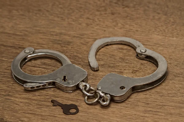 Closeup shot of metallic handcuffs on wooden background — Stock Photo, Image