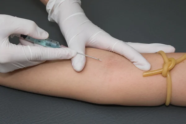 Brazo de mujer con un torniquete que se inyecta con una jeringa en — Foto de Stock