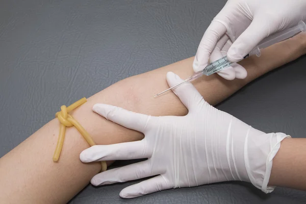 Woman arm with a tourniquet getting injection with a syringe at — Stock Photo, Image