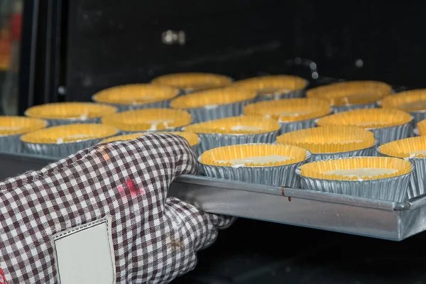 Mão da mulher colocando uma bandeja de bolo de xícara crua no forno — Fotografia de Stock