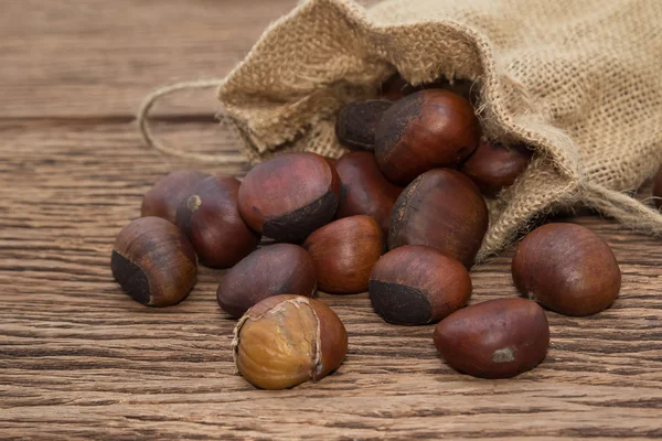 Geroosterde kastanjes in zak op houten achtergrond — Stockfoto