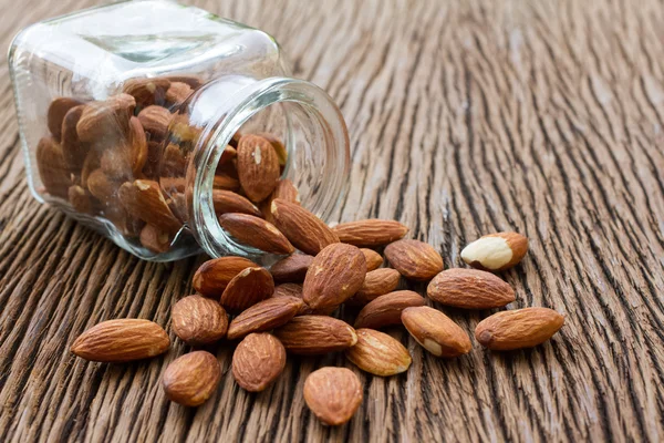 Les amandes coulent de la bouteille en verre sur la table en bois — Photo