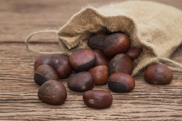 Geroosterde kastanjes in doek zak op houten achtergrond — Stockfoto