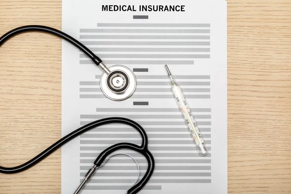 Stethoscope and thermometer laying on the blank of medical insur — Stock Photo, Image