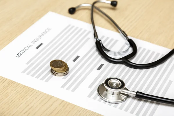 Stethoscope and coins laying on the blank of medical insurance. — Stock Photo, Image