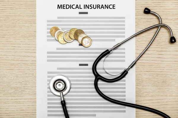 Stethoscope and coins laying on the blank of medical insurance. — Stock Photo, Image