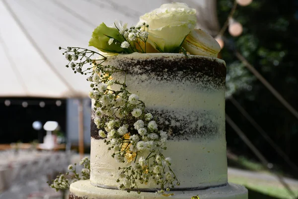 White gypsophila (or baby\'s breath) and white roses decorate the top tier of a white and chocolate wedding cake. A cream macaroon with yellow filling is among the flowers. The focus is on the foreground.