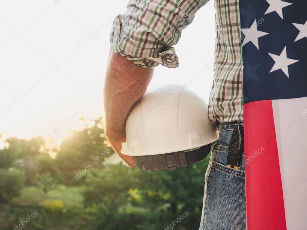 Attractive man in work clothes, holding tools in his hands against the background of trees, blue sky and sunset. View from the back. Labor and employment concept