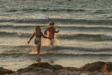 Şapkalı mutlu kızlar gün batımında denizde yüzerler. İsrail, Ashkelon 18 Ekim 2020