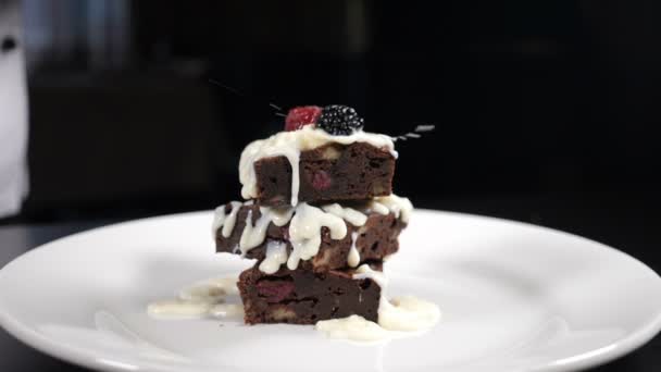 Pilha de sobremesa brownies que está sendo decorada com bagas na placa branca. Falling Berries em câmara lenta. Confeiteiro cozinhar deliciosa sobremesa na cozinha do restaurante. Fazendo sobremesa na casa de café — Vídeo de Stock