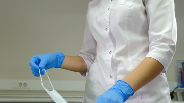 青い医療使い捨て手袋と白の均一な保持保護顔マスクの女性の手。科学者、医師または医療補助者の手による保護、医療用マスク。4 kビデオ — ストック動画