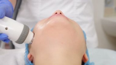 Güzellik salonunda cerrahi olmayan yüz gerdirme. makine kozmetolojisi. Yüz gerdirme cihazı flaşlar yapıyor. Yüz yenileme ameliyatı. Koruyucu gözlüklü bir kadının güzellik prosedürünü çekerken yakın plan fotoğrafı. 4 bin.