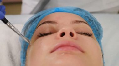 Profesyonel güzellik uzmanı yüz kremini fırçayla sürüyor. Güzellik kliniği. Genç bir kadın yüz bakımı yaptırıyor. Güzellik uzmanı kadın gözlerine maske takar. Yüzü yenilenmiş. 4k video