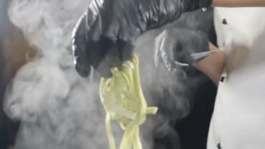 Siyah eldivenli şef kaynar suya çiğ makarna koyuyor. Beyaz duman ağır çekimde siyah arka planda sıcak tencerenin üzerinde yükseliyor. Restoranda yemek pişirmek. Lezzetli İtalyan makarnası. Tam Hd
