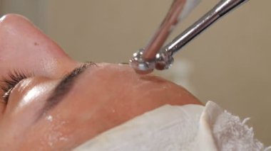 Kozmetolojide donanım prosedürü. Yakın plan. Güzellik kliniğinde cerrahi olmayan yüz gerdirme. Güzellik uzmanı kozmetikçi doktor yüzünü manipüle ediyor. Mikro akım tedavisi. 4k video