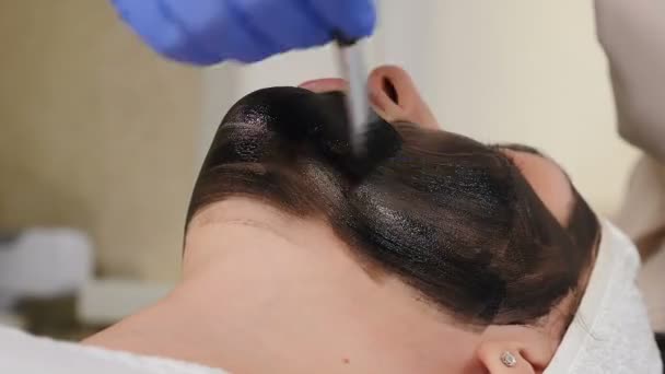 Carbon peeling. Hardware cosmetology. Facial skin rejuvenation. Preparation for cosmetic procedure in beauty clinic. Cosmetologist applies carbon compound on skin with brush. 4 k video — Stock Video