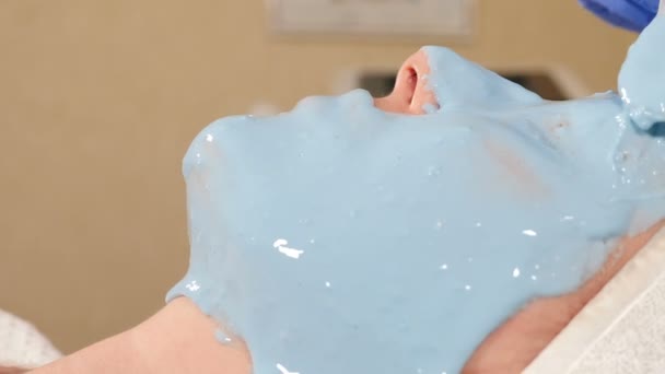 Cosmetologue applique un masque en alginate avec spatule sur le visage féminin. Soin visage et anti-âge. Cosmetologie et soins professionnels de la peau du visage. salon de beauté moderne. Vidéo 4 k — Video