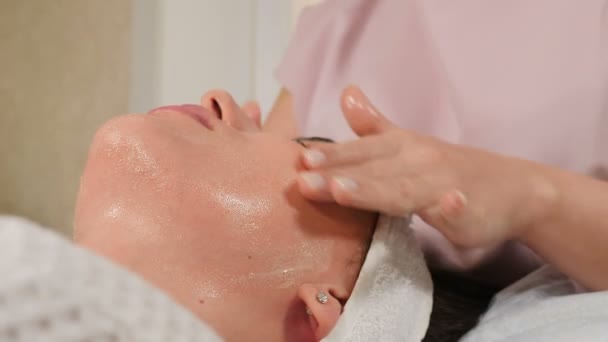 Bienestar y salón de belleza. Mujer relajada acostada en el sofá y con una limpieza profunda que nutre el tratamiento facial. esteticista haciendo masaje a cara femenina. Salud y medicina. 4 k vídeo — Vídeos de Stock