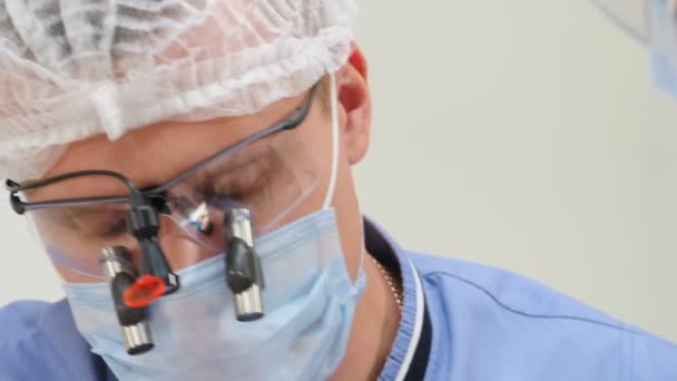 Concepto de cuidado dental y dental. gafas binoculares de aumento en el dentista masculino joven durante el tratamiento dental. ortodoncista en binocular en ojos haciendo cirugía dental. 4 k vídeo — Vídeos de Stock