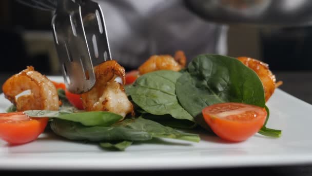 A mão põe o camarão na salada com pinças. Prato de acabamento Chef adicionando camarão frito ao aperitivo vegetariano fresco cozido na cozinha do restaurante. Movimento lento. servindo pratos no restaurante. Prato com camarão — Vídeo de Stock