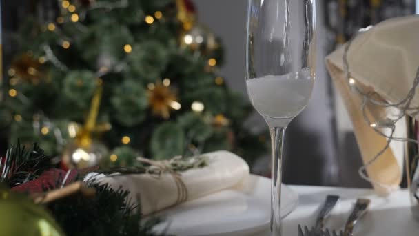 New Year holiday. Champagne being poured into glass on decorated feast table and Christmas tree with colorful twinkle garlands in background. Pouring Champagne in slow motion. Full hd — Stock Video
