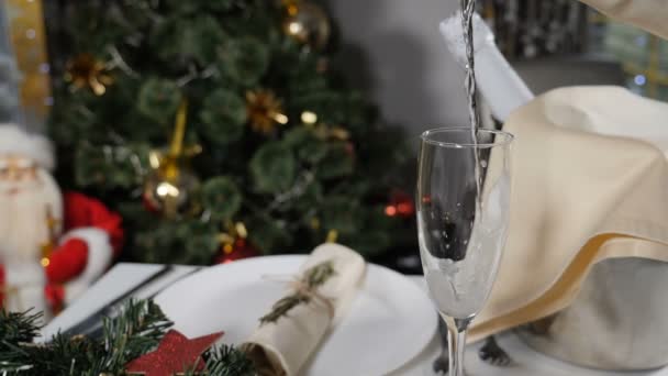 Vacaciones de Año Nuevo. Champán que se vierte en vidrio en la mesa de fiesta decorada y el árbol de Navidad con guirnaldas brillantes de colores en el fondo. Verter champán en cámara lenta. Full hd — Vídeos de Stock