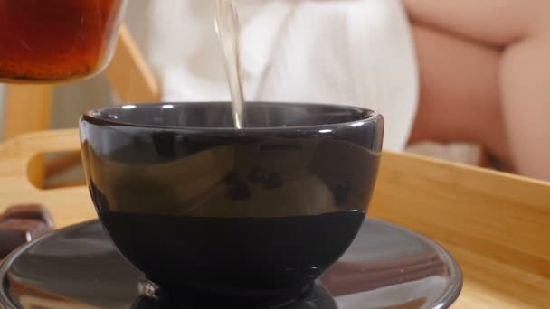 Травяной чай наливают в чашку в салоне спа-массажа с женскими ногами, покрытыми белым халатом на заднем плане. Красота и здоровье. заливка свежего зеленого чая после массажа. 4 k видео — стоковое видео