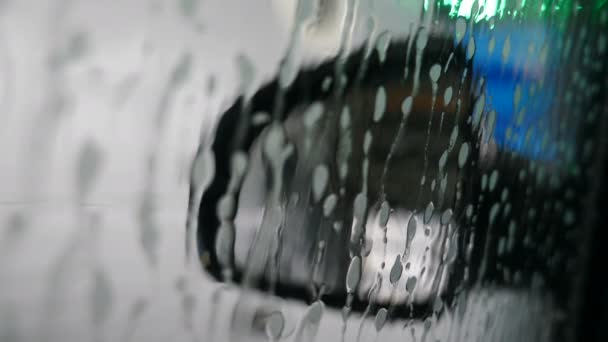 Lavadora de coches robótica. Vista en el espejo del coche desde el interior. Pequeñas gotas de detergente cayendo sobre la superficie del coche. servicio de lavado de coches en acción. 4 k vídeo — Vídeo de stock
