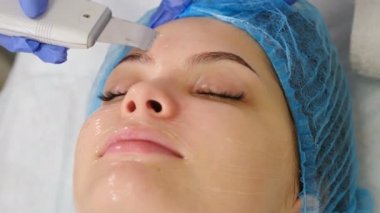 Güzellik kliniği ve makina kozmetolojisi. Profesyonel kozmetik uzmanı arınma işlemi sırasında ultrasonik yüz makinesiyle çalışıyor. Cerrahi olmayan yüz kaldırma. Dermatolog doktor. 4k video