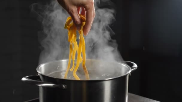 Female chef putting raw pasta into boiling water. White smoke in slow motion rising above hot saucepan on black background. Cooking in restaurant. Delicious Italian pasta. Full hd — Stock Video